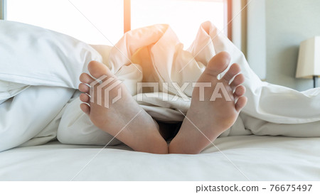Sleeping comfort, health relaxation, bedtime insomnia and world sleep day concept with young girl bare foot on bed lying lazy, resting in comfy hotel bedroom on white bed sheet 76675497