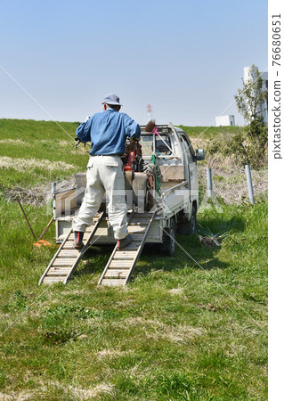 A man carrying a cultivator by truck A man carrying a cultivator by truck 76680651