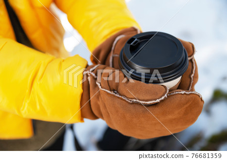 paper cup with a black lid in the hands of a woman in mittens paper cup with a black lid in the hands of a woman in mittens 76681359