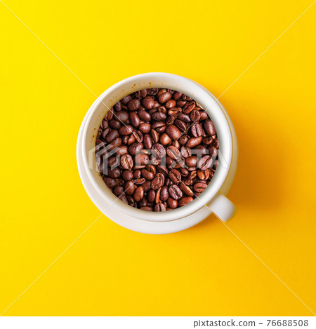Top view a white cup with coffee beans isolated on yellow background. Good morning time Top view a white cup with coffee beans isolated on yellow background. Good morning time 76688508