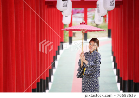 woman in kimono holding umbrella walking into at the shrine red gate, in Japanese garden. 76688639