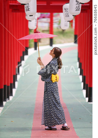 woman in kimono holding umbrella walking into at the shrine red gate, in Japanese garden. 76688645