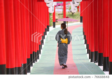 woman in kimono holding umbrella walking into at the shrine red gate, in Japanese garden. 76688648