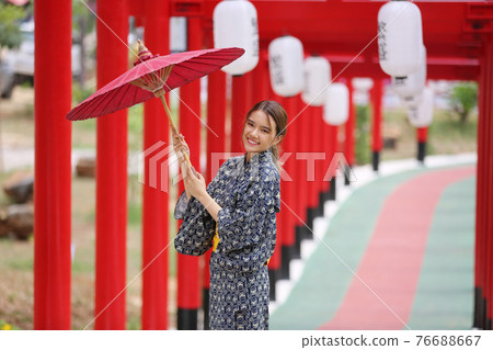 woman in kimono holding umbrella walking into at the shrine red gate, in Japanese garden. 76688667