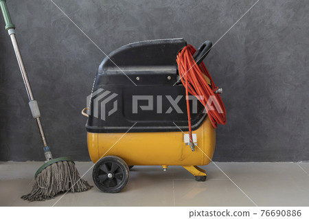 The electric air pumps with mop are placed on a gray tiled floor behind unpainted plaster walls. The electric air pumps with mop are placed on a gray tiled floor behind unpainted plaster walls. 76690886