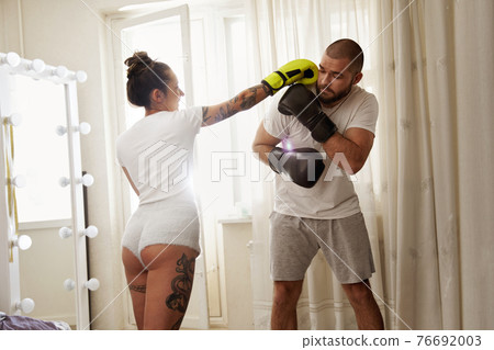 Woman wearing gloves doing hook to her boyfriend while having boxing training Woman wearing gloves doing hook to her boyfriend while having boxing training 76692003