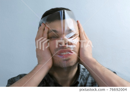 Portrait of man is puttion on plastic transparent film on his face. Portrait of man is puttion on plastic transparent film on his face. 76692004