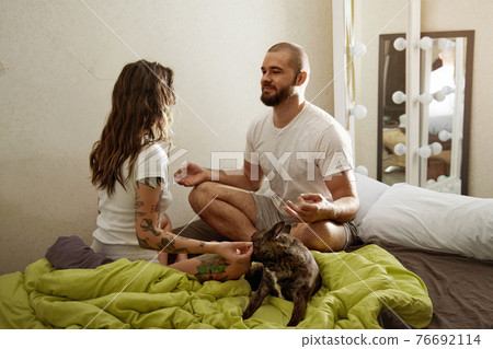 Couple practicing meditation exercises on the bed near their dog at home 76692114