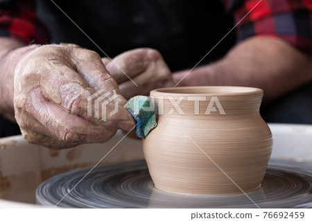 Male hands cleaning with sponge pottery on a potter wheel. Male hands cleaning with sponge pottery on a potter wheel. 76692459