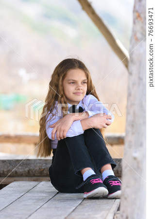 A girl sits on a wooden table and looks into the distance happily and dreamily 76693471