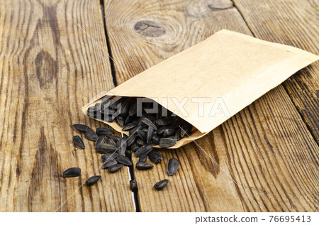 Black unpeeled sunflower seeds in craft bag on wooden table. 76695413