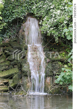 Waterfall over stones into pond 76695674