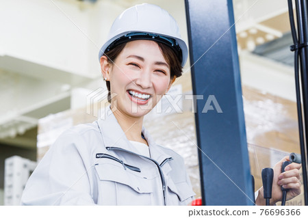 A woman wearing a helmet and operating a forklift 76696366