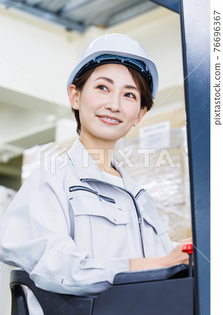 A woman wearing a helmet and operating a forklift A woman wearing a helmet and operating a forklift 76696367