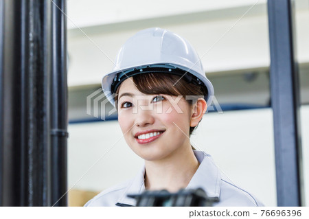 A woman wearing a helmet and operating a forklift 76696396