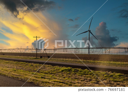 Water sprinkler system in a green field at sunset with wind turbines windmill energy farm in Texas USA Water sprinkler system in a green field at sunset with wind turbines windmill energy farm in Texas USA 76697181
