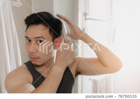 Man is combing his hair in the bathroom. Man is combing his hair in the bathroom. 76700310