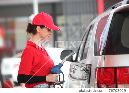 woman with red uniform at the gas station for service , young woman refuel the car or Young girl with fuel pump nozzle at modern gas station 76702029