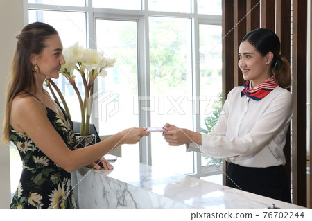 Happy young woman at hotel reception receiving the key of the room. 76702244