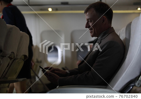 businessman in airliner working on his computer while talking by cellphone , Young handsome businessman with notebook sitting inside an airplane businessman in airliner working on his computer while talking by cellphone , Young handsome businessman with notebook sitting inside an airplane 76702840