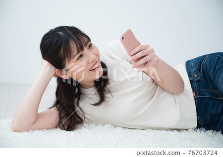 A woman lying on a carpet and looking at her smartphone A woman lying on a carpet and looking at her smartphone 76703724