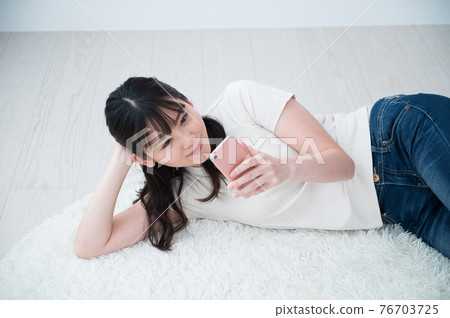 A woman lying on a carpet and looking at her smartphone 76703725