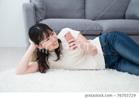 A woman lying on a carpet and looking at her smartphone A woman lying on a carpet and looking at her smartphone 76703729