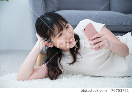 A woman lying on a carpet and looking at her smartphone A woman lying on a carpet and looking at her smartphone 76703731