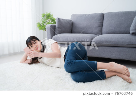 A woman lying on a carpet and looking at her smartphone A woman lying on a carpet and looking at her smartphone 76703746