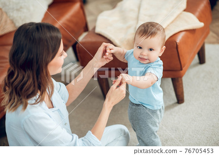 Smiling baby standing holding moms hands 76705453