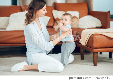 Woman sitting on floor supporting child with hands Woman sitting on floor supporting child with hands 76705519