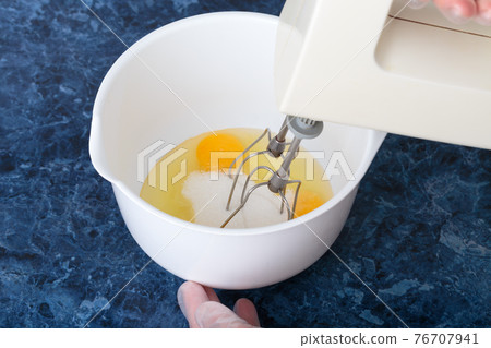 A blender whips eggs and sugar in a bowl. A blender whips eggs and sugar in a bowl. 76707941