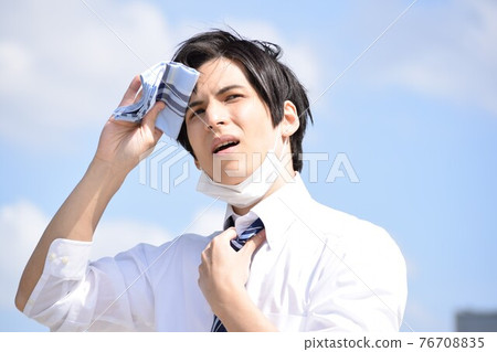 一個熱的年輕人摘下口罩用手帕擦汗 76708835