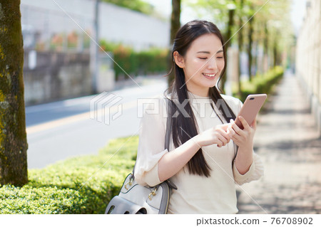 College student with a smartphone in front of the campus College student with a smartphone in front of the campus 76708902