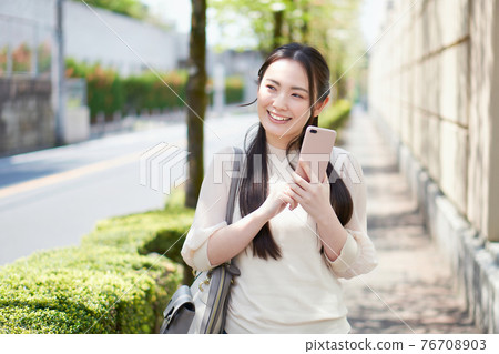 College student with a smartphone in front of the campus College student with a smartphone in front of the campus 76708903