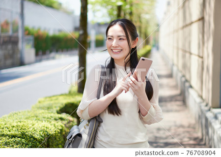 College student with a smartphone in front of the campus College student with a smartphone in front of the campus 76708904