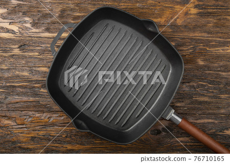 An empty black cast iron grill pan for cooking delicious meat. Wood background. Space for text. An empty black cast iron grill pan for cooking delicious meat. Wood background. Space for text. 76710165