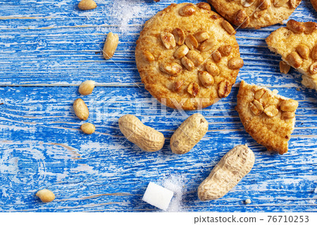 Peanut cookies on a blue wooden background. Sugar and peanuts in a peel are scattered on the table. 76710253