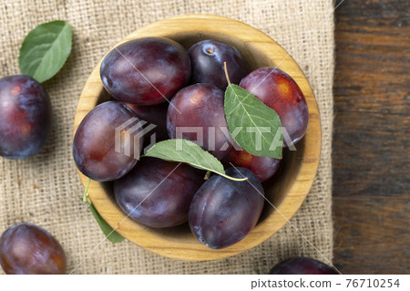 Ripe plums and leaves in a wooden bowl on the table. 76710254