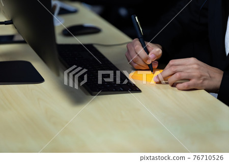 Close up image of businessman writing on an adhesive note at table in office. Close up image of businessman writing on an adhesive note at table in office. 76710526