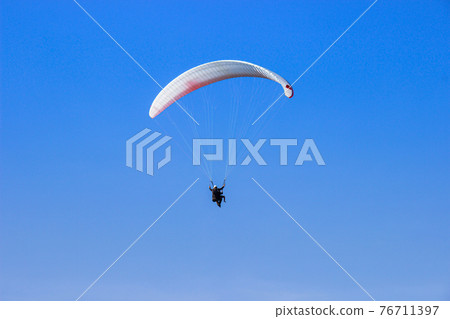 Tourist flying on a paraglider flying in the blue sky on a bight day. The sportsman paragliding. 76711397