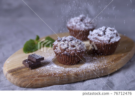 Chocolate muffins on a wooden board, strewed with icing sugar. Homemade baking. Selective focus, close up. 76712476