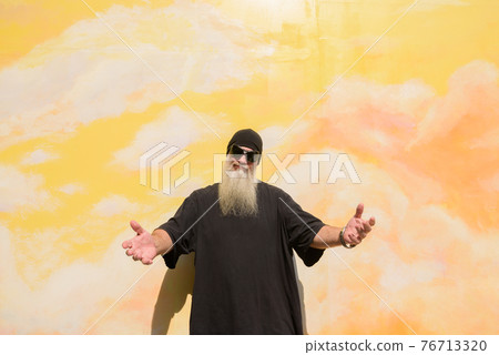 Summer portrait of mature man with long gray beard against cloudy background wall with open arms 76713320
