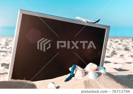 Summer holiday poster. Globe, seashell, airplane and starfish near black desk on sea beach in sunny day. Summer vacation and product advertisement concept. Summer holiday poster. Globe, seashell, airplane and starfish near black desk on sea beach in sunny day. Summer vacation and product advertisement concept. 76713794