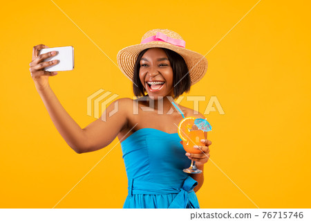 Happy black woman with yummy summer cocktail taking selfie on smartphone over orange studio background Happy black woman with yummy summer cocktail taking selfie on smartphone over orange studio background 76715746