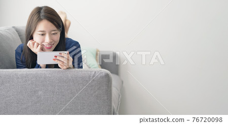 一個女人躺在沙發上,看著她的智能手機 一個女人躺在沙發上,看著她的智能手機 76720098