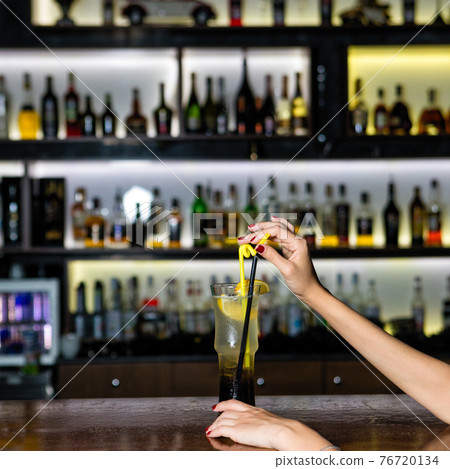 Woman holding lemon fruit cocktail at the bar 76720134