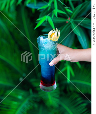 Woman holding blue colored cocktail with green background Woman holding blue colored cocktail with green background 76720139