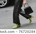 Detail of a fashionable outfit woman wearing green shoes, black handbag and black leather pants 76720284
