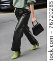 Detail of a fashionable outfit woman wearing green shoes, black handbag and black leather pants 76720285